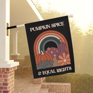 May include: A black rectangular garden flag featuring the text PUMPKIN SPICE & EQUAL RIGHTS in white. The design includes a multi-colored rainbow, a round orange pumpkin, a purple gourd, a large orange flower, and small floral accents.