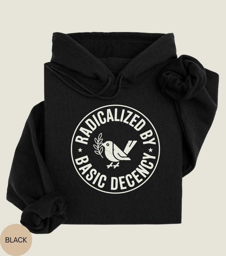 May include: Black hoodie with a white circular graphic that reads "RADICALIZED BY BASIC DECENCY" around a bird holding a sprig. The hoodie has a drawstring hood and long sleeves. The word "BLACK" is in a tan circle in the lower left corner.