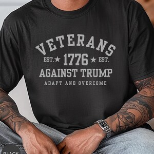 Puede incluir: Camiseta negra con el texto gris "VETERANS EST. 1776 EST. AGAINST TRUMP ADAPT AND OVERCOME". La camiseta es de cuello redondo.