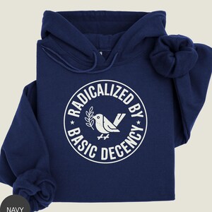 May include: Navy blue hoodie with a white graphic. The graphic is a circle with the words "RADICALIZED BY BASIC DECENCY" surrounding a bird holding a sprig. The hoodie has a drawstring hood and a front pocket.