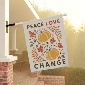 May include: A rectangular garden flag featuring the text PEACE LOVE CHANGE in dark brown and red. The design includes two yellow pumpkins surrounded by brown vines, red and orange autumn leaves, and small red berries on a light cream background.