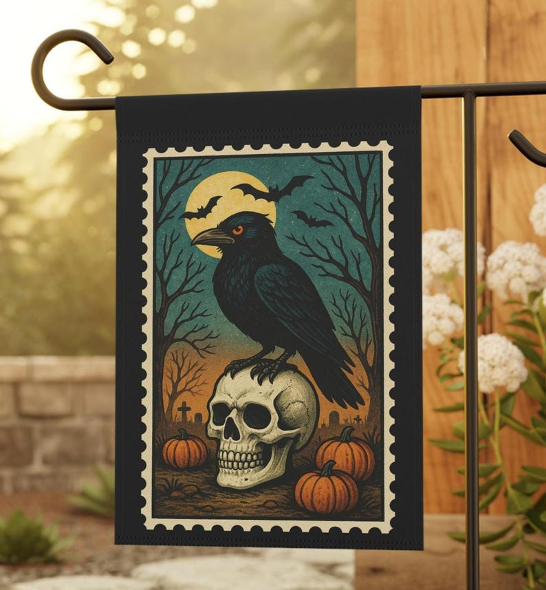 May include: Black Halloween garden flag featuring a raven perched on a skull, with pumpkins, bats, and a full moon. The design has a vintage, postage stamp style with a black border. The flag is displayed outdoors.