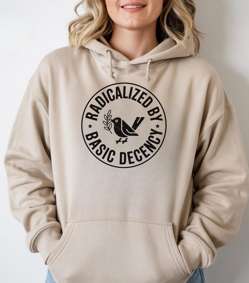 May include: Beige hoodie with a black circular graphic that reads "RADICALIZED BY BASIC DECENCY" around a bird holding a sprig. The hoodie has a drawstring hood and a front pocket.