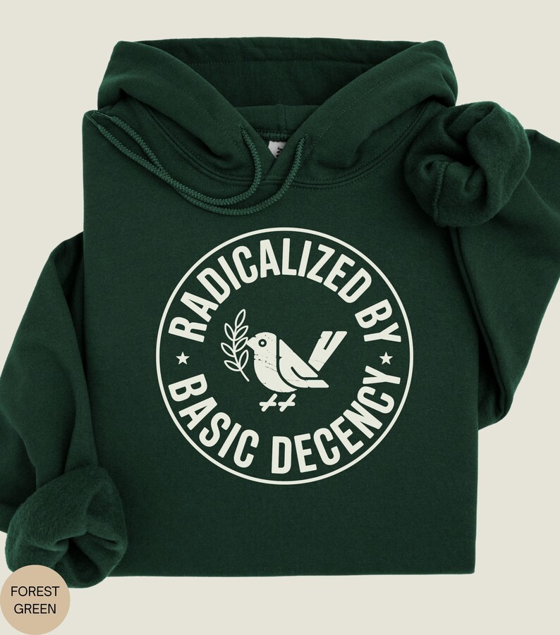 May include: Forest green hoodie with a white graphic. The graphic is a circle with the words "RADICALIZED BY BASIC DECENCY" around a dove holding a sprig. The hoodie has a drawstring hood and a kangaroo pocket.