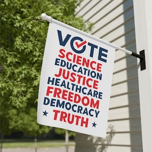 May include: A white flag with the word "VOTE" in navy blue with a red checkmark, and the words "SCIENCE, EDUCATION, JUSTICE, HEALTHCARE, FREEDOM, DEMOCRACY, TRUTH" in red. The flag is hanging on a white wall.