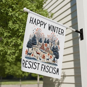 May include: A white flag with the words "HAPPY WINTER" and "RESIST FASCISM" in black. The flag features a winter scene with deer, trees, and small buildings in shades of blue, red, and brown. The flag is mounted on a white pole.