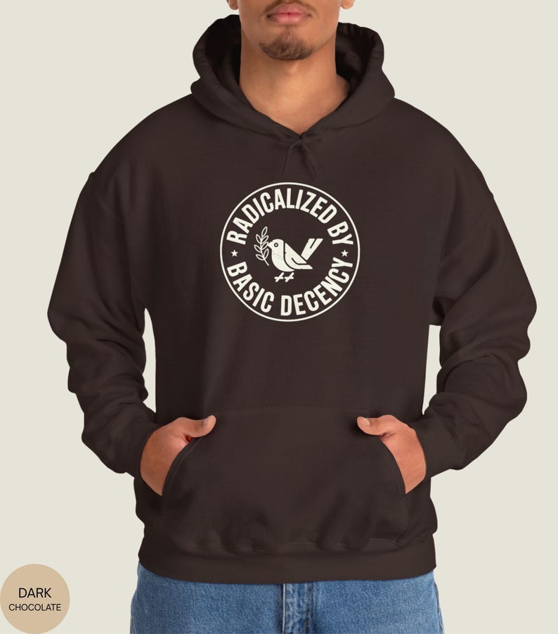 May include: Dark chocolate-colored hoodie with a white circular graphic that reads "RADICALIZED BY BASIC DECENCY" around a bird and olive branch design. The hoodie has a hood and a front pocket.