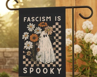 May include: Black garden flag with the text "FASCISM IS SPOOKY" in white. The flag features a ghost illustration with a bouquet of daisies and orange flowers. A checkered pattern is on the right side of the flag.