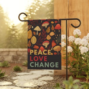 Peut inclure: Un drapeau de jardin rectangulaire suspendu à un support en métal noir. Le drapeau présente un fond sombre avec un motif de champignons colorés et de feuilles d'automne. Le texte PEACE en jaune, LOVE en rouge et CHANGE en vert clair est imprimé.