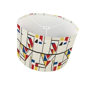 May include: A cream-colored lampshade with a geometric pattern in red, yellow, blue, and black. The design features angular shapes and lines. The lampshade has a white interior and a metal frame.