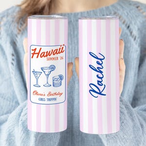 May include: Two pink and white striped tumblers. One has a label with "Hawaii Summer '26" and cocktail illustrations. The other has the name "Rachel" in blue script. The tumblers are designed for Olura's Birthday and are ideal for drinks.