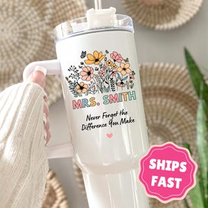 May include: White tumbler with a floral design and the text "MRS. SMITH Never Forget the Difference You Make." The design includes butterflies, flowers, and leaves in pastel colors. The tumbler has a handle and a clear lid.