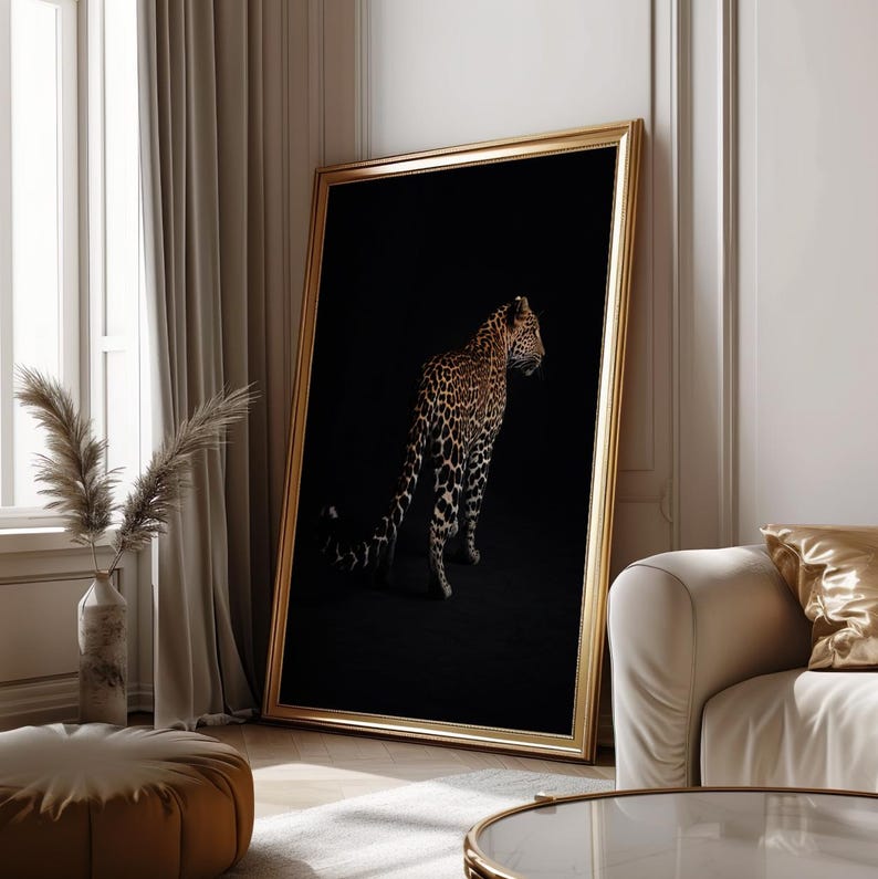 May include: A black and white photograph of a leopard standing in a dark room. The leopard is facing to the right and its tail is curled behind it. The photograph is framed in a gold frame.