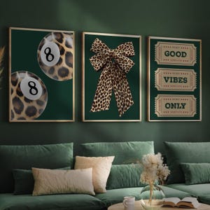 May include: Three framed art prints with gold frames. The left print features two eight balls with a leopard print design. The center print displays a leopard print bow. The right print has three tickets that read "Good Vibes Only."