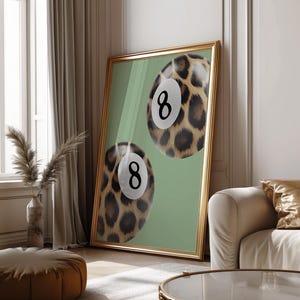 May include: Two 8-ball billiard balls with a leopard print design on a green background. The balls are framed in a gold frame.