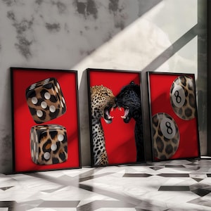 May include: Three framed art prints with a red background. One print features two dice with a leopard print pattern. Another print shows a leopard and a black panther snarling at each other. The third print displays two leopard-print eight-ball pool balls.