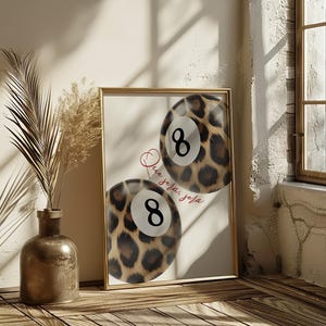 May include: Two 8-ball pool balls with a leopard print design. The text "Que seja: seja" is written in red cursive on a white background.