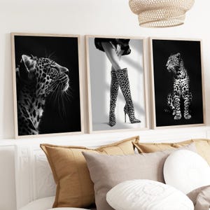 May include: Three black and white prints featuring a leopard, a woman wearing leopard print boots, and a leopard cub. The prints are framed in a light wood frame.