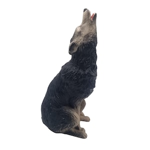 Puede incluir: Figura de un lobo aullando, representado en posición sentada con la cabeza levantada y la boca abierta. El lobo tiene pelaje negro en la espalda y los costados, con la cara y el pecho de color gris claro. El interior de la boca es de color rojo-rosado.