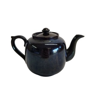 May include: A dark blue ceramic teapot with a shiny glaze. The teapot has a rounded body and a spout on the right side. The handle is on the left side and is attached to the body of the teapot.