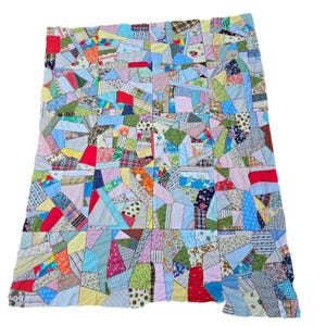 May include: A patchwork quilt composed of various fabric scraps in a vibrant array of colors and patterns. The quilt features geometric shapes and a mix of floral, plaid, and solid fabrics, creating a unique and colorful textile.
