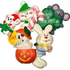May include: A collection of whimsical, colorful figurines featuring holiday and seasonal themes. Includes a Christmas mouse with a candy cane, a Halloween ghost in a pumpkin, a bunny with an Easter egg, and a mouse holding a shamrock with "Luck O' The Irish" text.