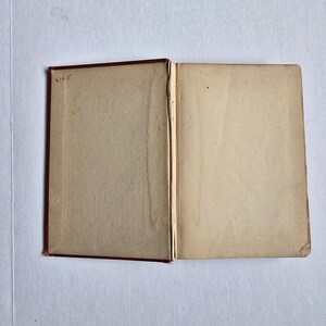 Peut inclure: Un livre ouvert avec des pages vieillies de couleur cr&egrave;me. La couverture est rouge fonc&eacute; et le dos est visible. La page de gauche porte l'inscription manuscrite "814 E" dans le coin sup&eacute;rieur gauche. Le livre est ouvert sur une surface blanche.