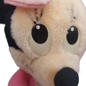 Puede incluir: Un juguete de peluche de un rat&oacute;n de dibujos animados con ojos grandes, un lazo rosa y una nariz negra. El juguete est&aacute; hecho de piel suave y blanca.