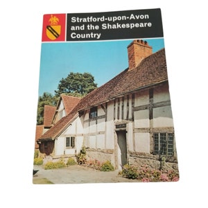 Pode incluir: Um cartão postal vintage com uma casa branca de estrutura de madeira com telhado marrom. A casa é cercada por árvores verdes e flores. O texto no cartão postal diz "Stratford-upon-Avon and the Shakespeare Country."