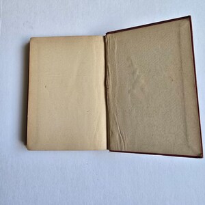 Peut inclure: Un livre ouvert avec des pages jaunies de couleur cr&egrave;me. La couverture du livre est rouge fonc&eacute; et les pages montrent des signes d'usure. Le livre est &agrave; plat, les pages ouvertes, r&eacute;v&eacute;lant l'int&eacute;rieur.