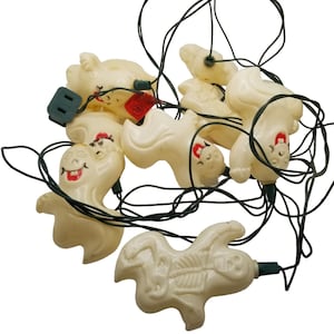May include: A string of white ghost-shaped Christmas lights with red smiling faces. The lights are connected by a green wire.