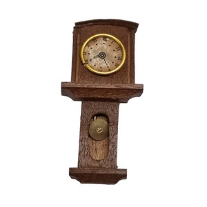 May include: A wooden grandfather clock with a gold-colored face and black hands. The clock has a pendulum and is a decorative piece.