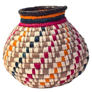 Puede incluir: Una cesta tejida a mano con un cuerpo redondeado y un borde ligeramente ensanchado. La cesta presenta un patrón vibrante de colores alternos, incluyendo blanco, marrón, naranja, rosa y azul marino. El borde es marrón oscuro con bandas naranjas, azul marino y rosa.