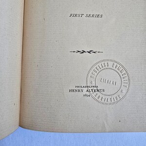 Peut inclure: Page de livre ouverte avec du texte et un tampon circulaire. Le texte "FIRST SERIES" est en haut. En dessous, une ligne d&eacute;corative et un tampon circulaire avec "DOUGLASS COMMUNITY LIBRARY ASSOCIATION" et "PHILADELPHIA HENRY ALTEMUS 1894".