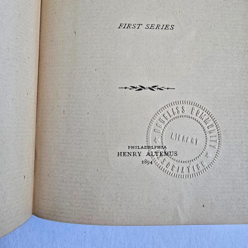 Peut inclure: Page de livre ouverte avec du texte et un tampon circulaire. Le texte "FIRST SERIES" est en haut. En dessous, une ligne d&eacute;corative et un tampon circulaire avec "DOUGLASS COMMUNITY LIBRARY ASSOCIATION" et "PHILADELPHIA HENRY ALTEMUS 1894".
