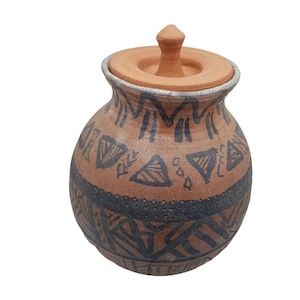 May include: A brown ceramic jar with a lid, decorated with black geometric patterns. The jar has a rounded body and a small, pointed lid.