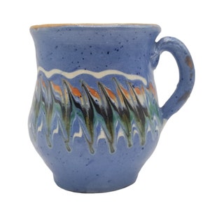 Pode incluir: Uma caneca de cerâmica azul com uma borda branca e um padrão de redemoinho de verde, preto e laranja. A caneca tem um corpo arredondado e uma alça.