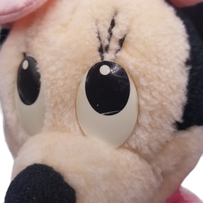 Puede incluir: Primer plano de un juguete de peluche con un sombrero rosa y grandes ojos negros. El juguete tiene una cara blanca y una nariz negra.