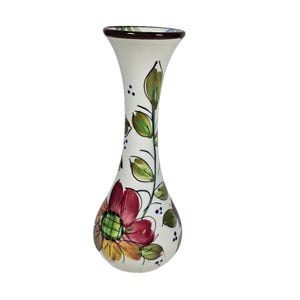 May include: A white ceramic vase with a flared top and a bulbous base. The vase is hand-painted with a red, yellow, and green floral design and green leaves. The rim is brown, and the vase is approximately 8 inches tall.