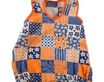 May include: A patchwork baby romper in orange, white, and navy blue. The romper features a variety of floral and geometric patterns, with snap closures at the bottom and button closures at the shoulders. The trim is orange.