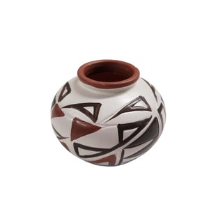 Puede incluir: Una pequeña maceta redonda de cerámica blanca con un borde marrón. La maceta está decorada con un patrón geométrico de triángulos negros y marrones.