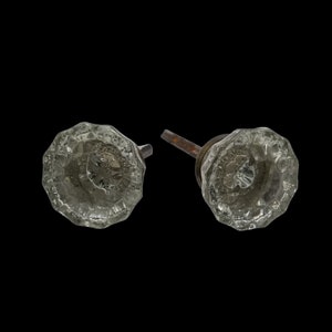 May include: Two antique glass door knobs with a faceted design and metal stems. The knobs are clear glass with a slightly frosted appearance.