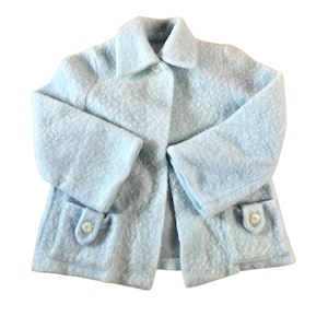 May include: A light blue coat with a textured, bouclé fabric. The coat features a classic collar, two front pockets with decorative buttons, and a single button closure. The sleeves are long, and the coat is likely for outerwear.