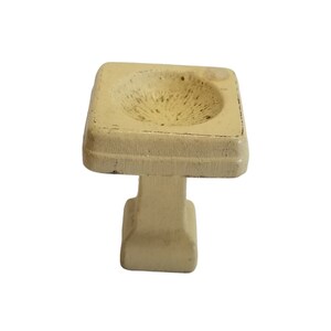 May include: A small, white, ceramic bird bath with a square top and a round base.