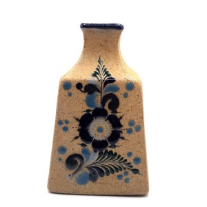 May include: A small, tan ceramic vase with a blue and green floral design. The vase has a square base and a narrow neck.