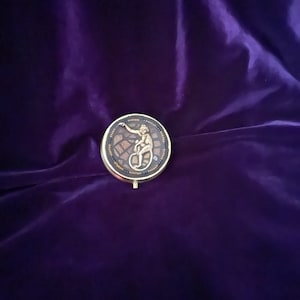 May include: A small, round, gold-colored trinket box with a mosaic design featuring a small, gold-colored figure of a monkey sitting on a circle.