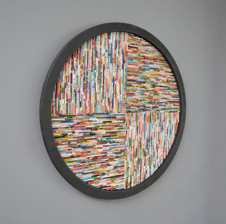 May include: A circular wall art piece made of rolled magazine paper in a variety of colours. The paper is arranged in a geometric pattern and framed in black.