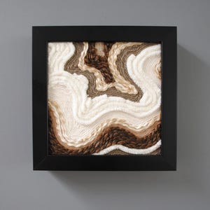 May include: A framed wall art piece with a textured design of swirling brown, beige, and white yarn.