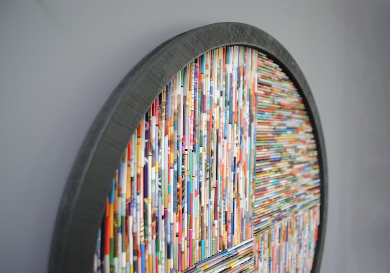 May include: A circular wall art piece made from colourful magazine strips, framed in a dark grey wood frame.