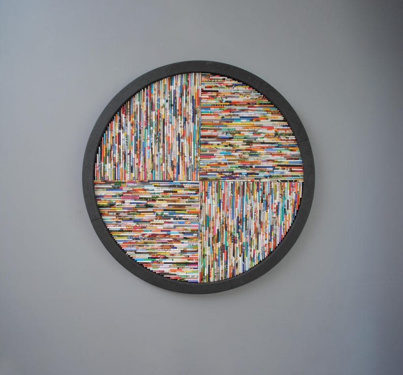 May include: A round wall art piece made of colourful magazine strips arranged in a geometric pattern. The strips are glued together to form a circular shape with a black frame.